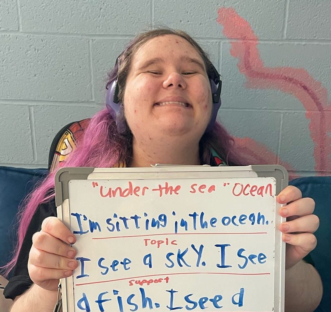 A young woman who is a student at Red Line Advocacy poses for the camera while proudly displaying her work, a poem she's written about the ocean.